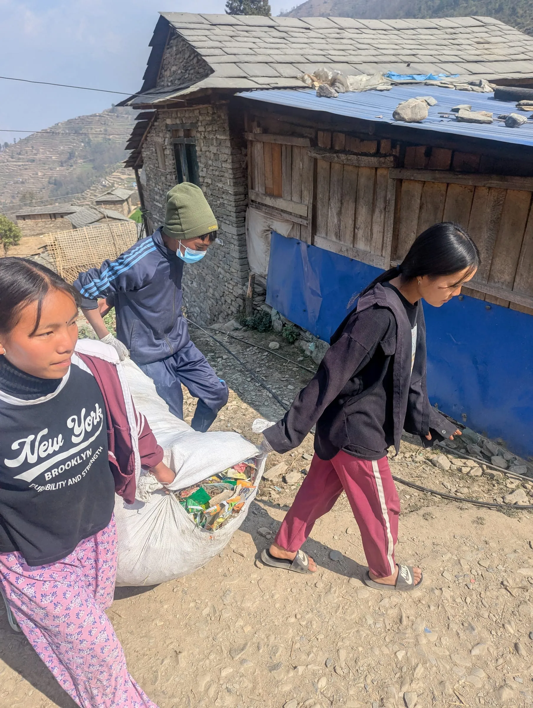 Two girls carrying a full sack of waste between them down a village lane.