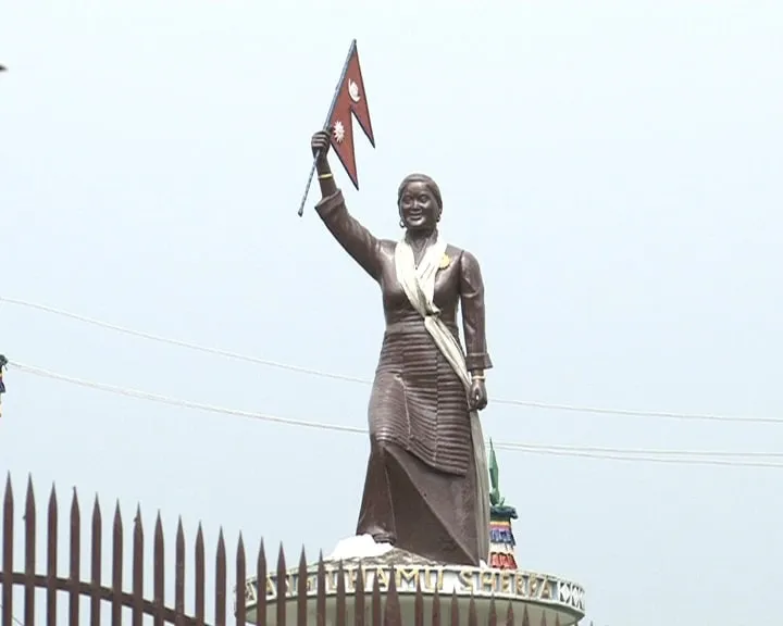 A bronze statue of Pasang Lhamu Sherpa raising the flag of Nepal, standing on a plinth behind iron railings against an open sky.