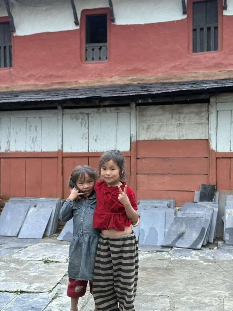 Two small children from Ruma standing together in front of a painted village wall.