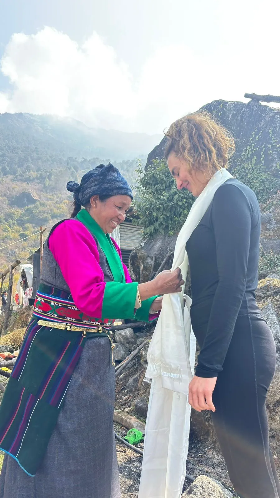 A village woman placing a ceremonial scarf around a visitor in greeting.