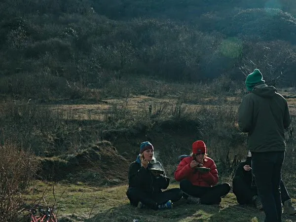 Two of the group sitting on the grass at their camp, cooking gear between them.
